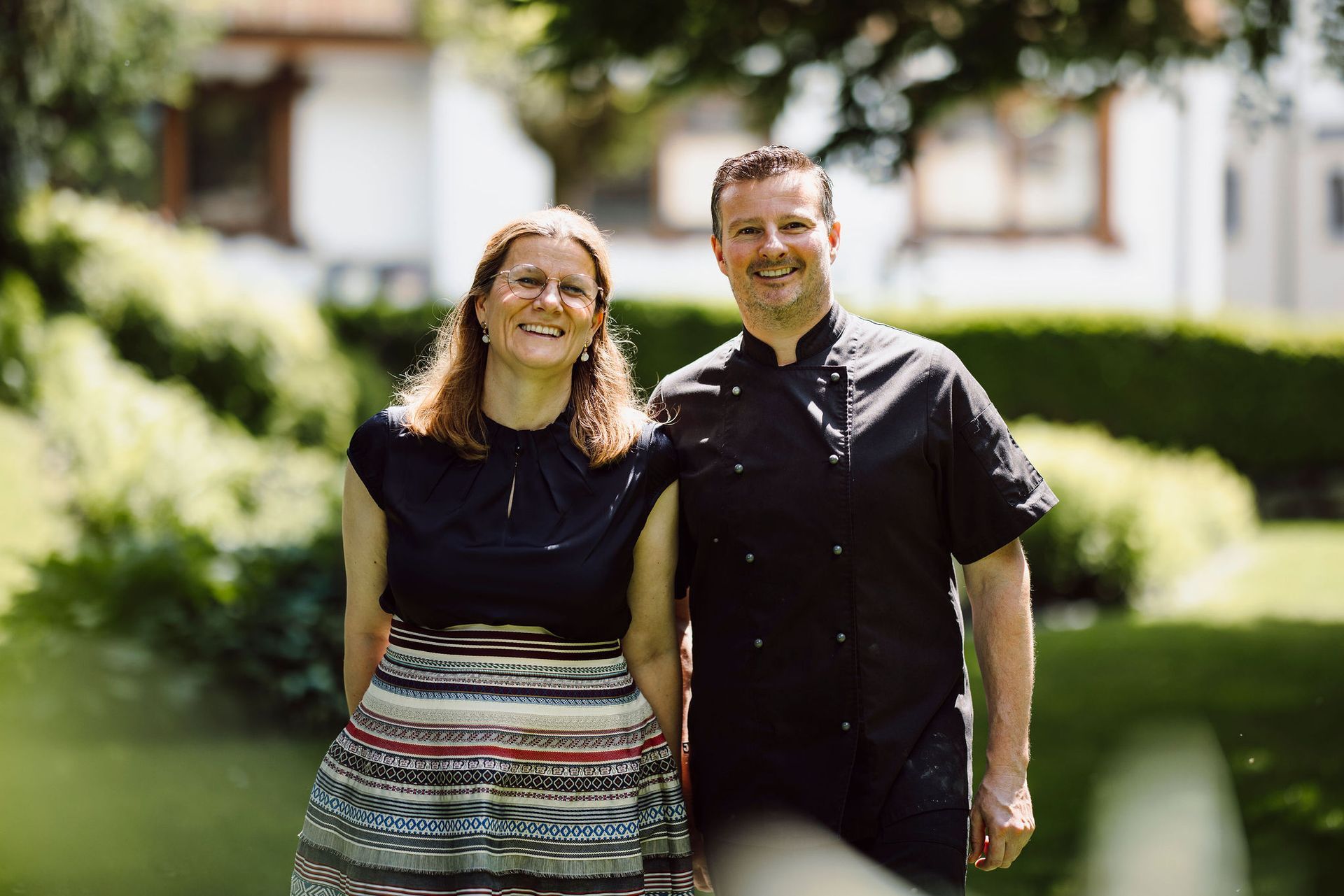 Ein Mann und eine Frau stehen nebeneinander lächelnd 
vor dem Hotel.