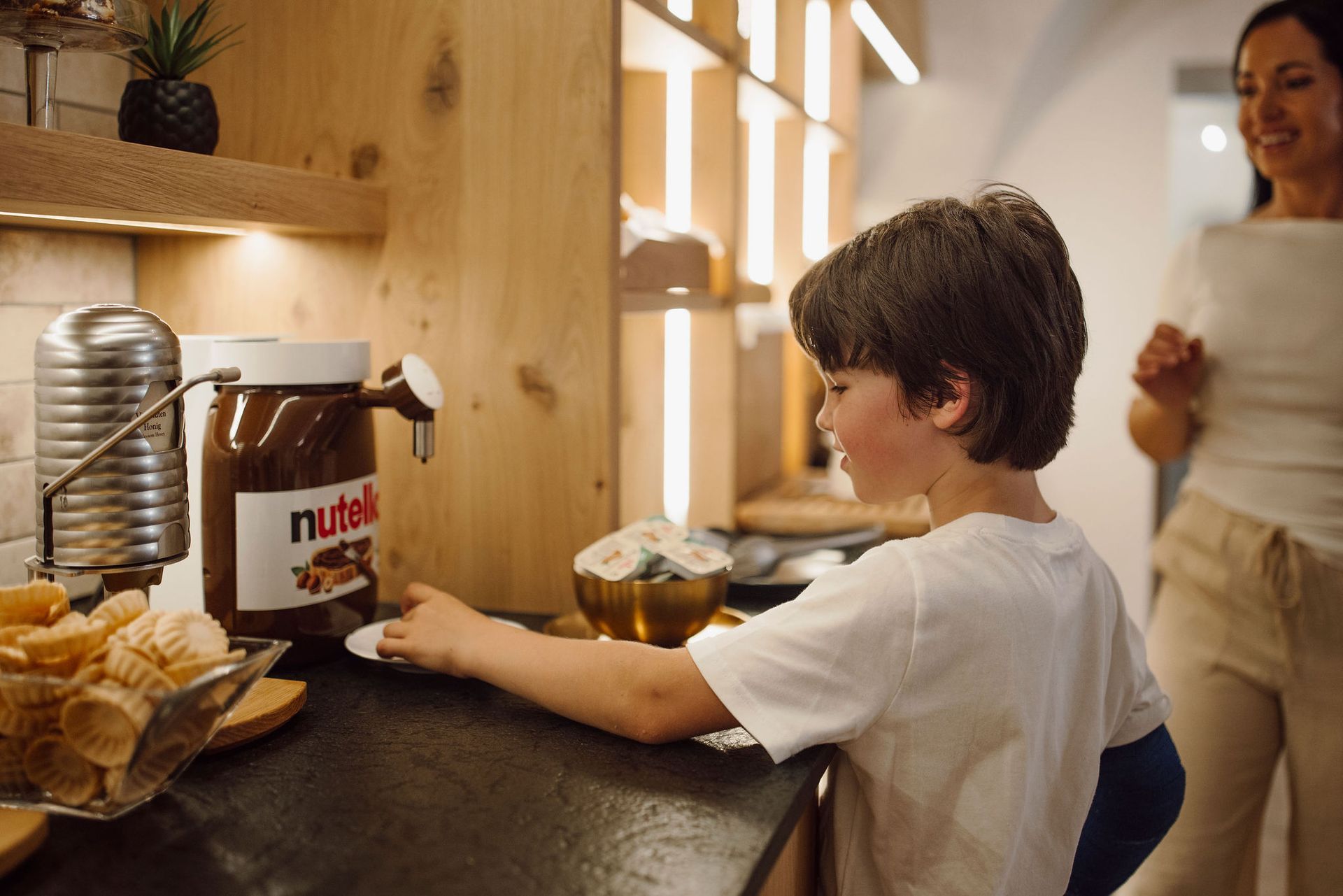 Ein kleiner Junge steht an einer Theke neben einem Glas Nutella.