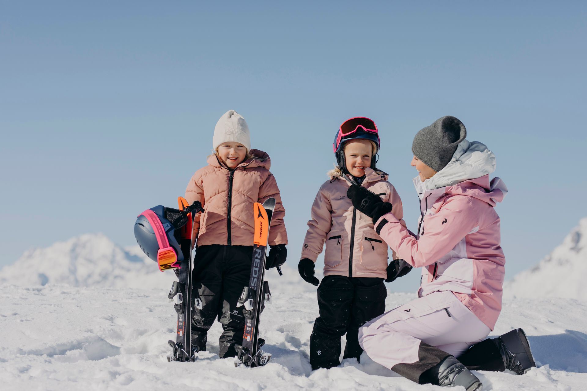 Eine Frau kniet neben zwei Kindern im Schnee.
