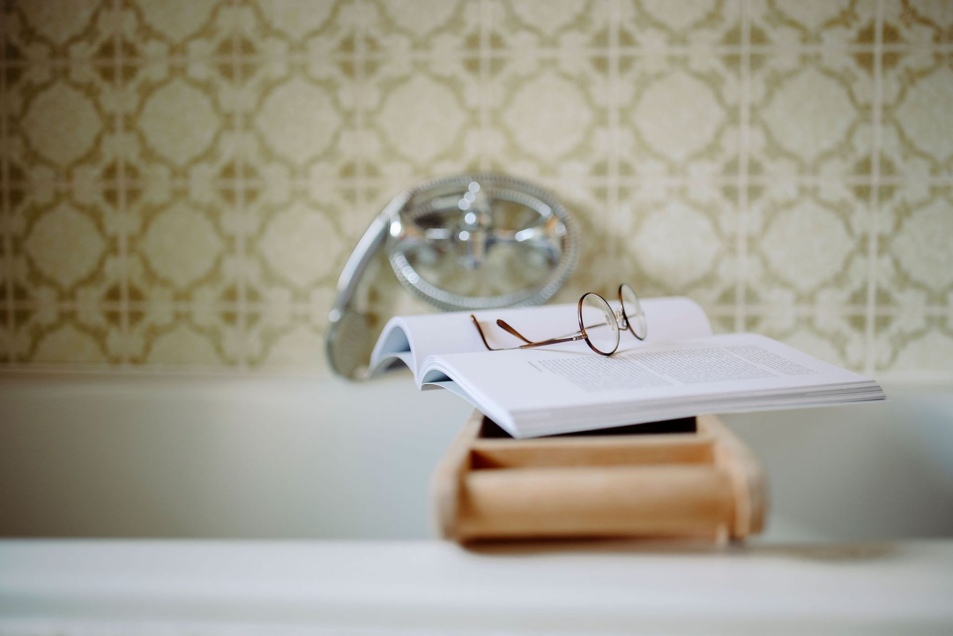 Ein Buch und eine Brille liegen auf einem Badewannentablett.