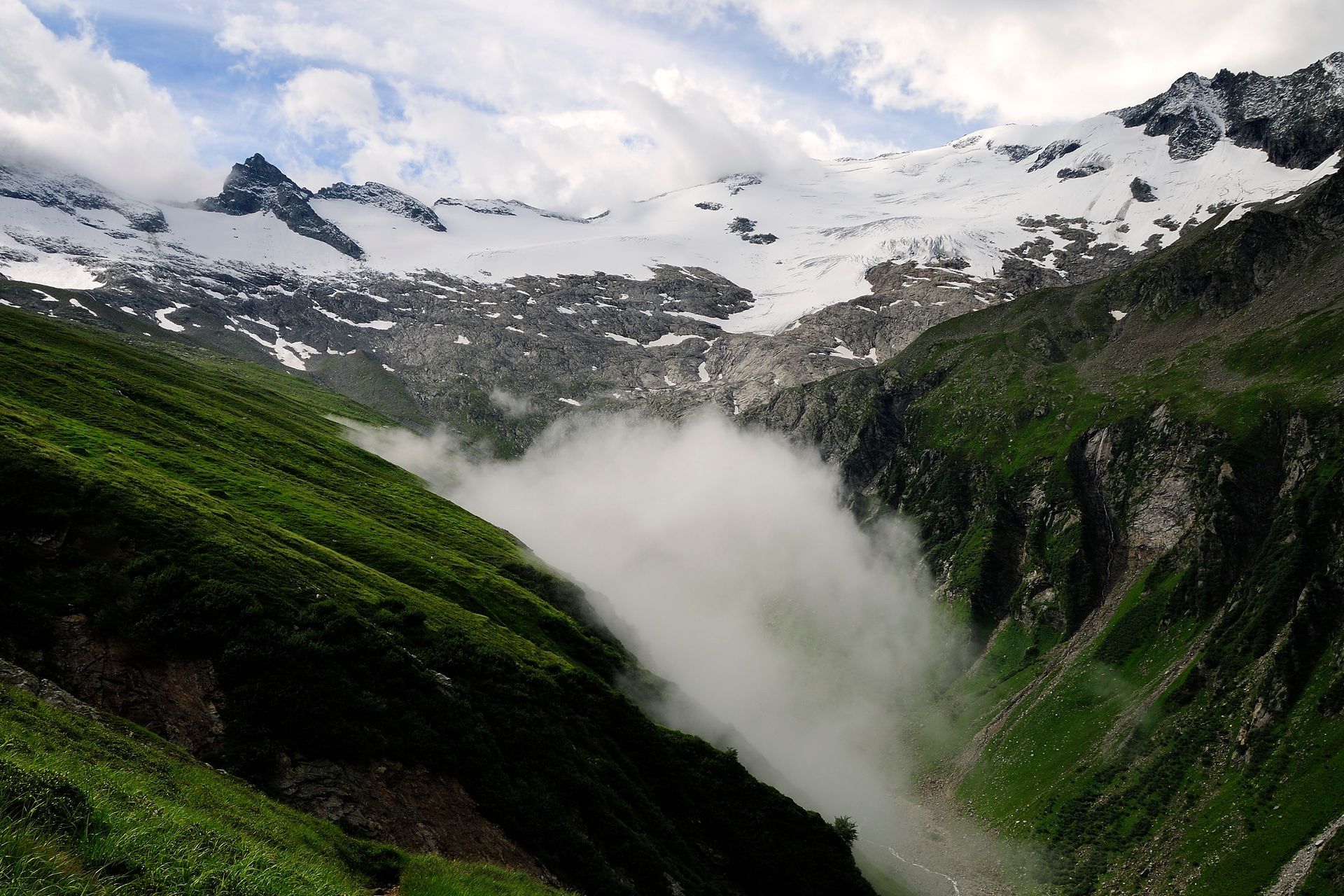 Ein Tal mit Bergen im Hintergrund und Wolken im Vordergrund