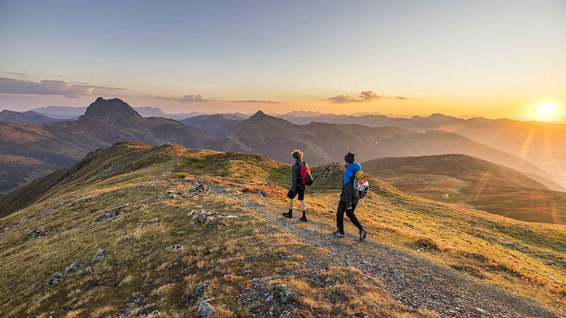 Zwei Personen wandern bei Sonnenuntergang auf einen Berg.