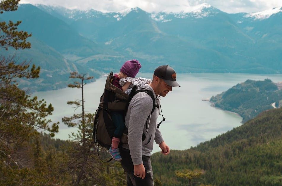 Ein Mann trägt ein Baby in einem Rucksack auf einem Berg.