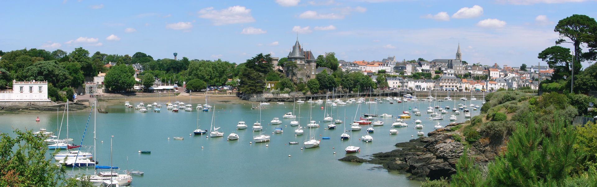 Port avec bateaux et château au bord de l'eau entouré d'arbres