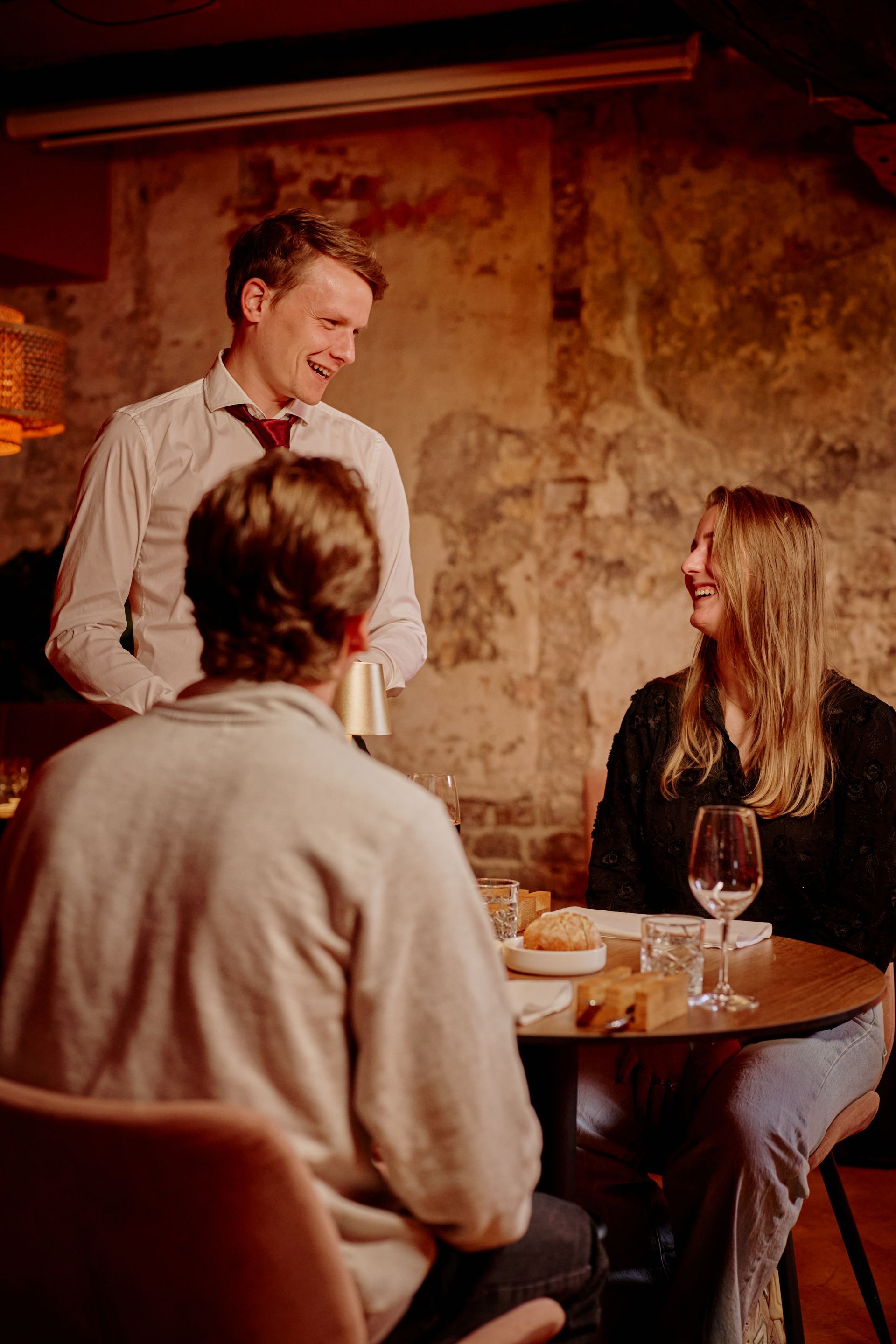 Een ober schenkt een drankje in voor een stel aan een tafeltje in een restaurant.