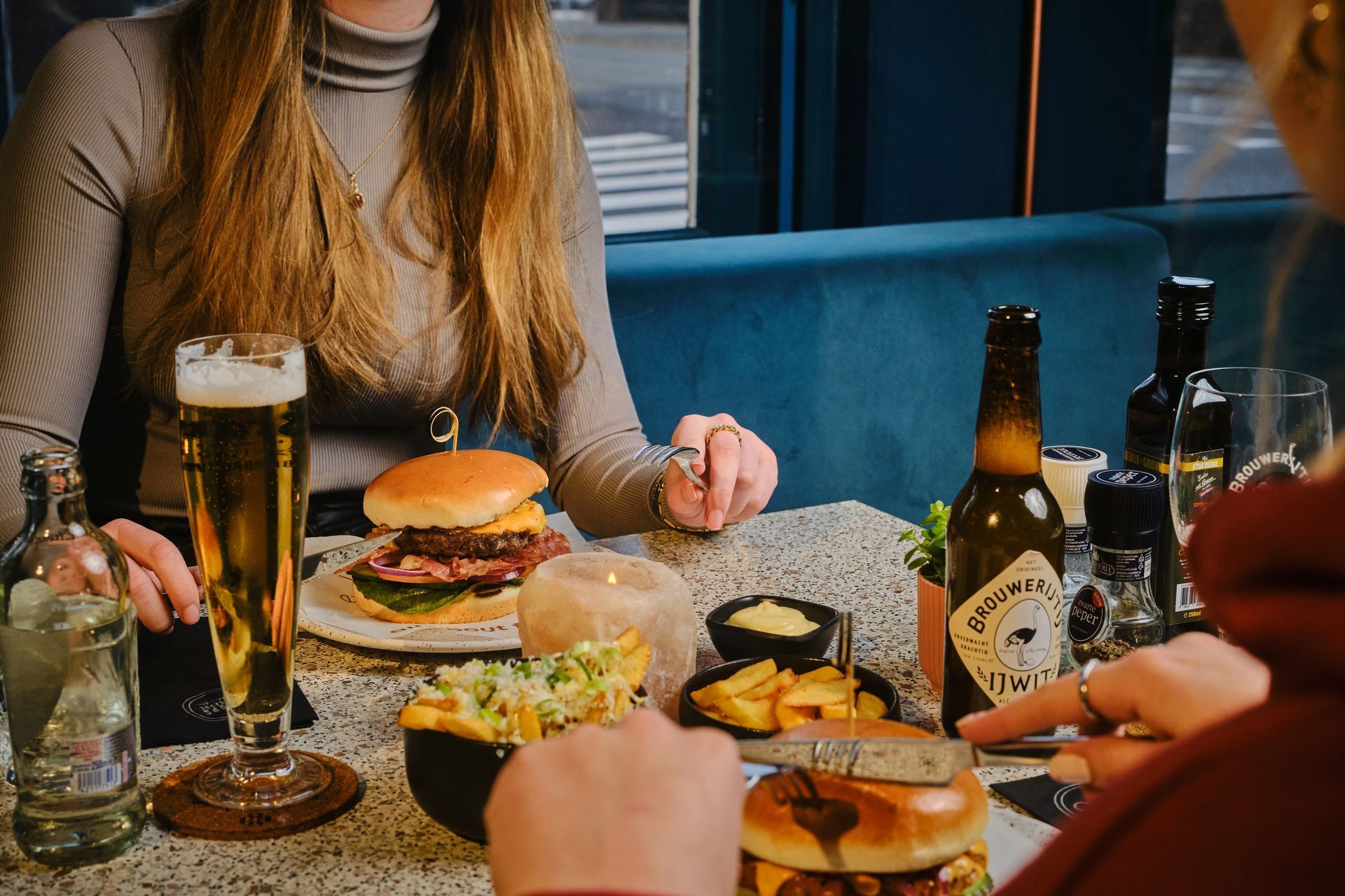 Zwei Frauen sitzen mit Burgern und Bier an einem Tisch.