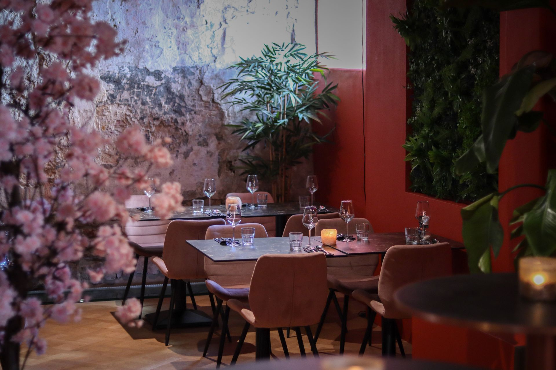 Een ober schenkt een drankje in voor een stel aan een tafeltje in een restaurant. De setting is modern, met planten en decoratieve verlichting.