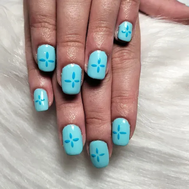 Uñas de color azul claro con un diseño de estrella de cuatro puntas de color azul más oscuro en el centro de cada uña.