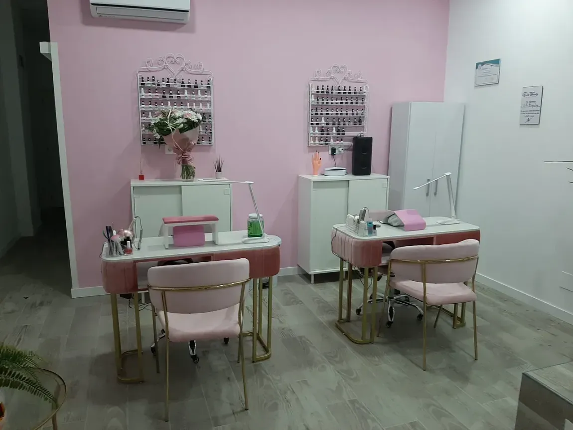 Un salón de uñas rosa con dos estaciones de manicura, sillas y gabinetes.