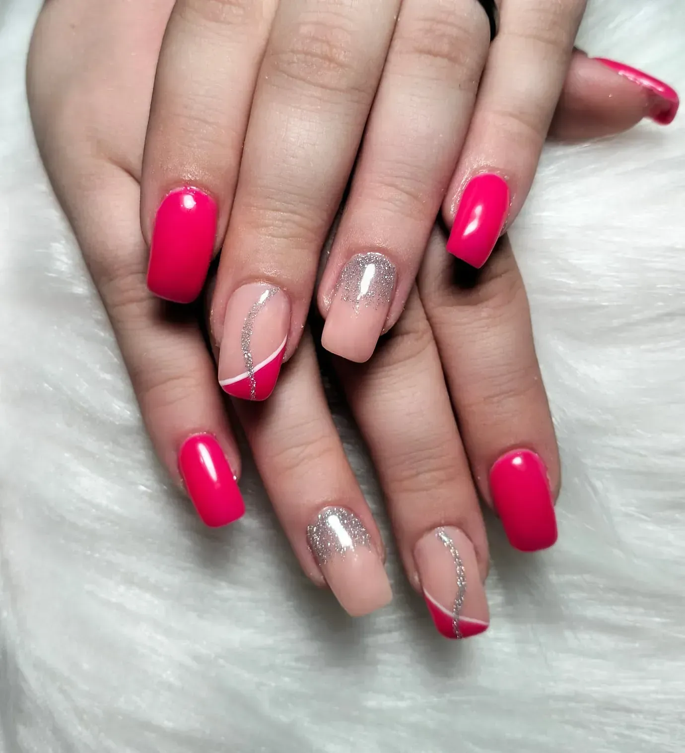 Manos con uñas pintadas de rosa y colores neutros. Algunas uñas tienen purpurina plateada o líneas blancas.