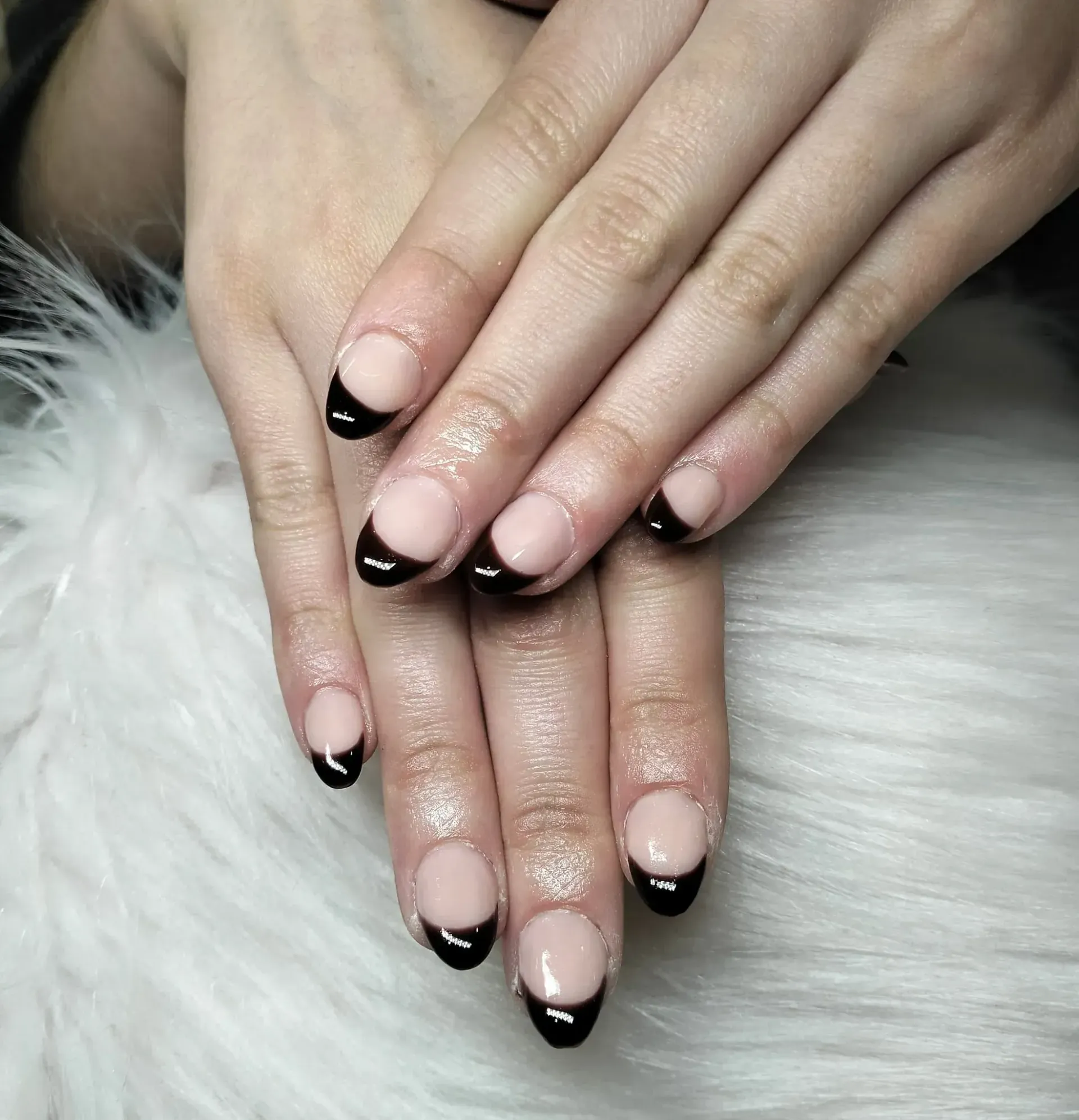 Manos con uñas en forma de almendra, estilo manicura francesa, puntas negras, sobre una superficie peluda blanca.