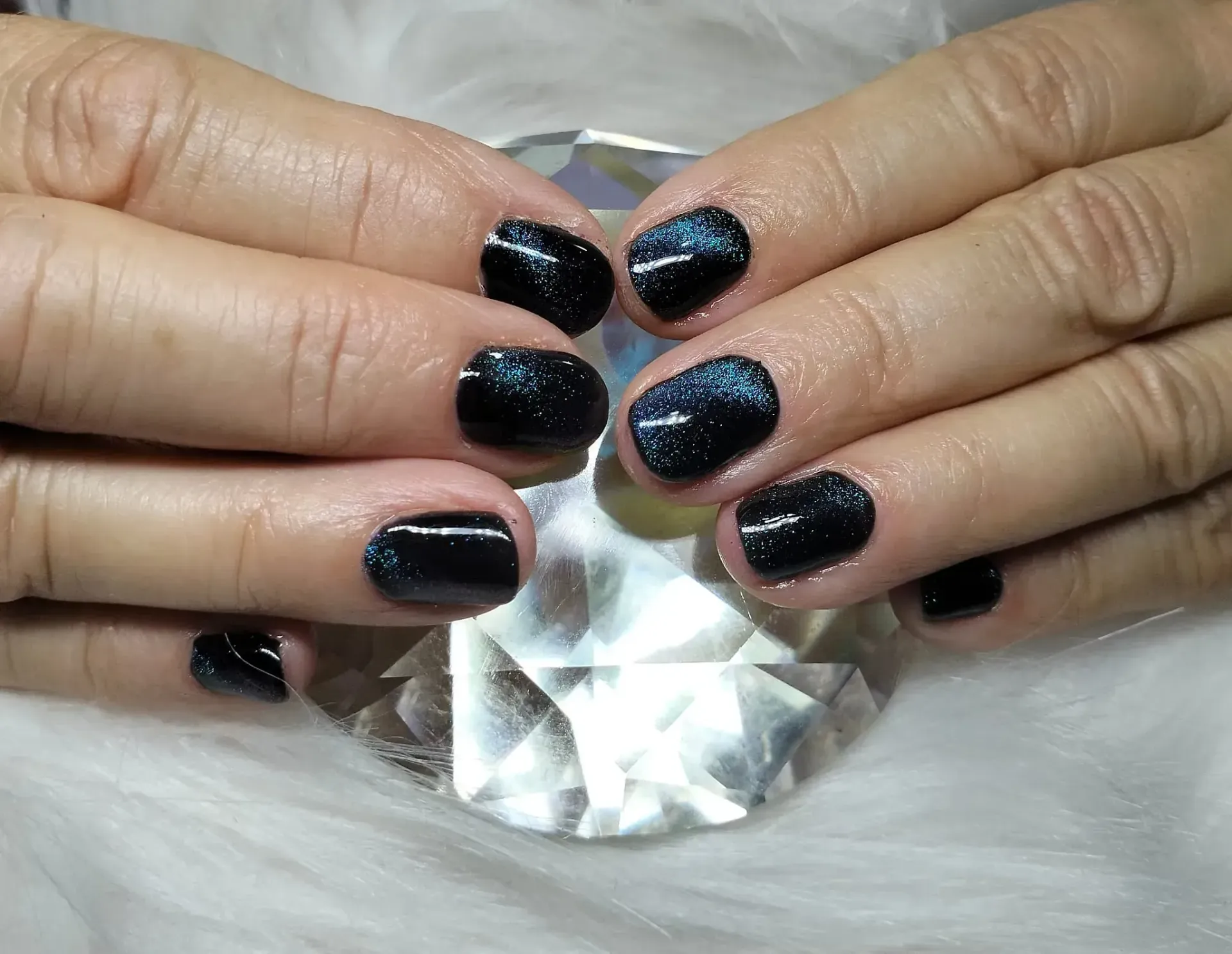 Manos con uñas cortas, oscuras y brillantes que descansan sobre un cristal facetado.