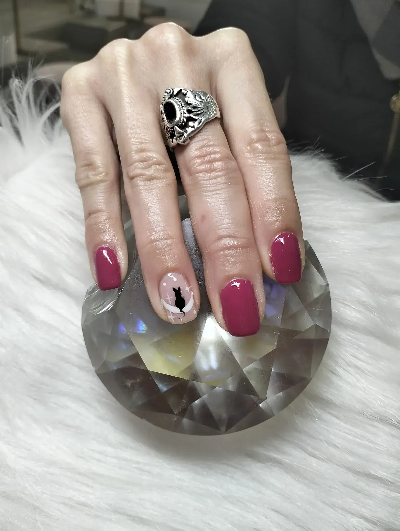 Mano con uñas de color granate y diseño de gato, sosteniendo una bola de cristal sobre pelaje blanco.