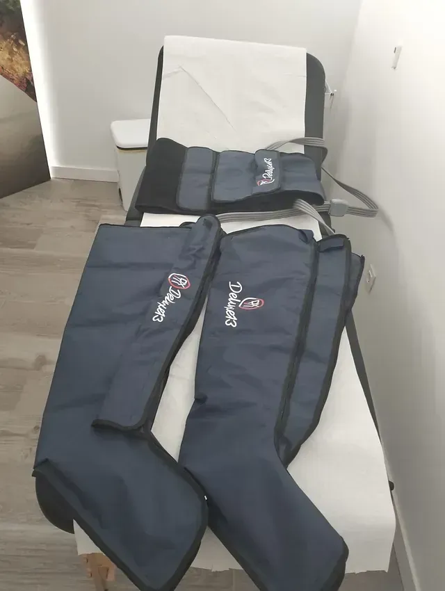 Botas de compresión azules y faja de cintura sobre una mesa de examen médico, posiblemente para drenaje linfático.