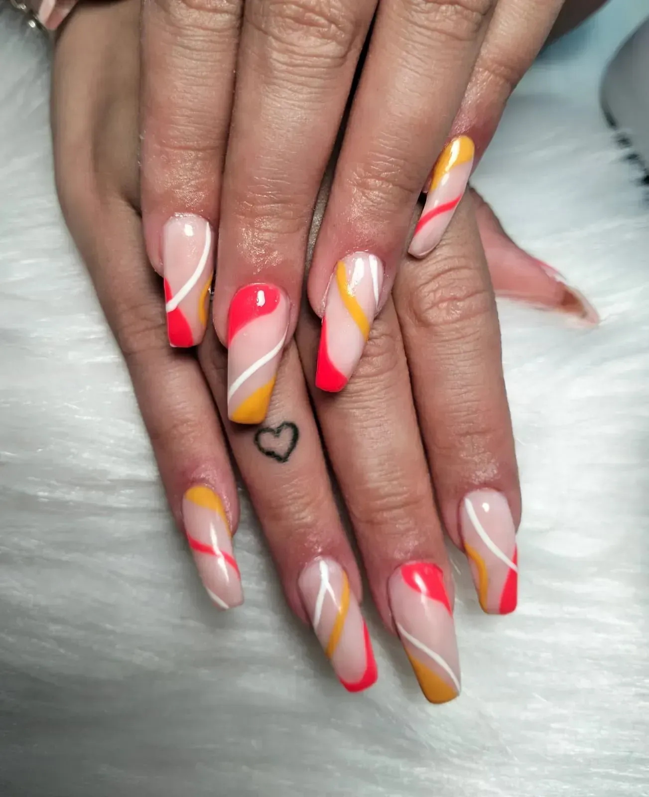 Uñas en forma de ataúd con diseños abstractos en rojo, amarillo y blanco sobre una mano tono piel.