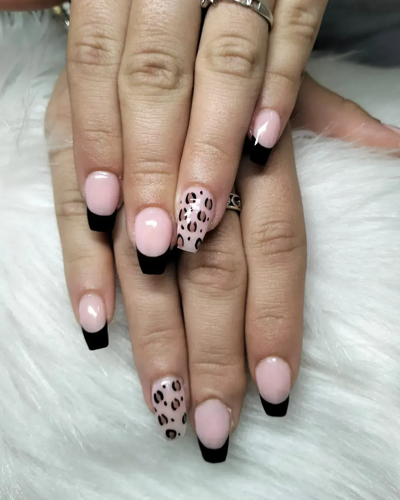Manos con uñas rosas, puntas francesas negras y uñas con detalles de estampado de leopardo sobre una superficie blanca difusa.