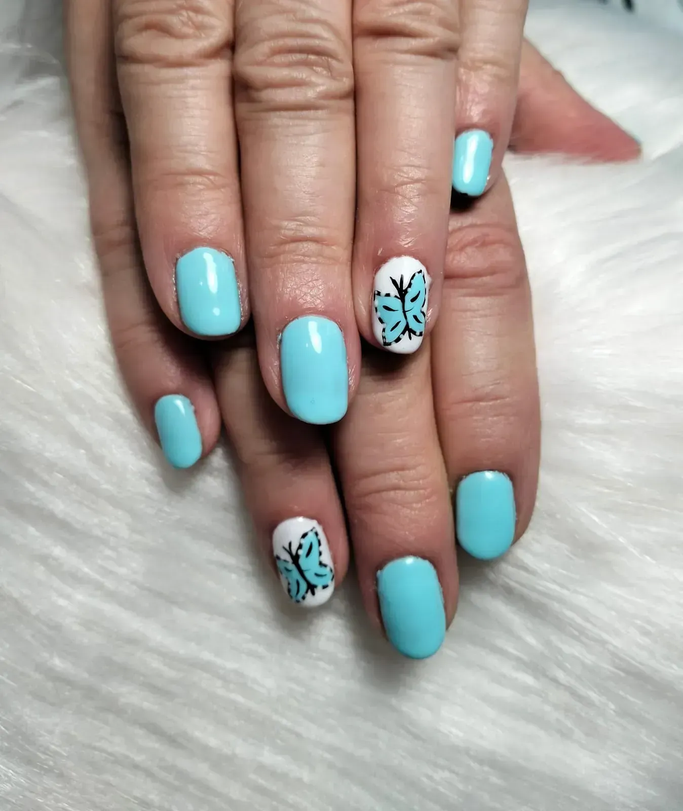 Uñas cuidadas en turquesa y blanco con detalles de mariposas.
