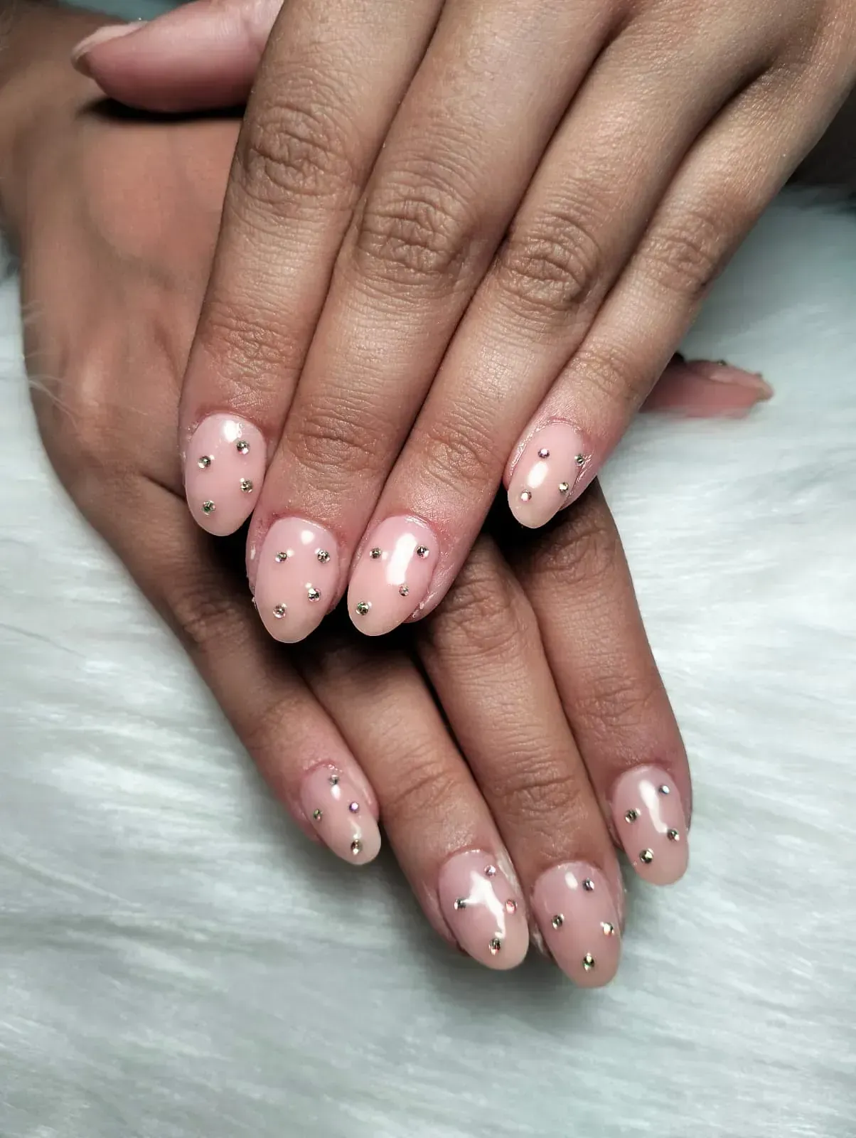 Uñas cuidadas con esmalte rosa claro y tachuelas plateadas.