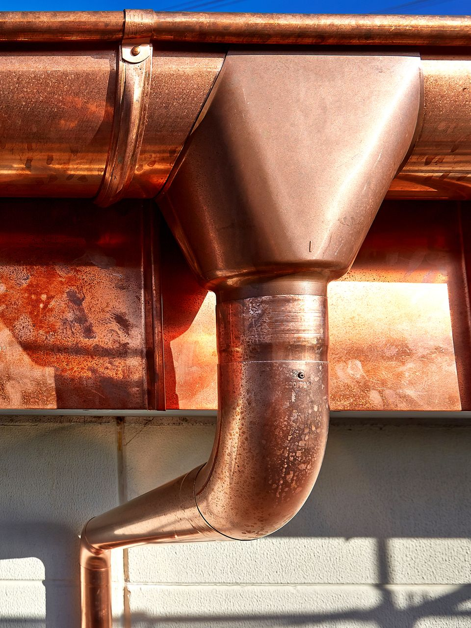Gouttière et descente pluviale en cuivre sur la façade d'un bâtiment, avec un coude à angle droit.