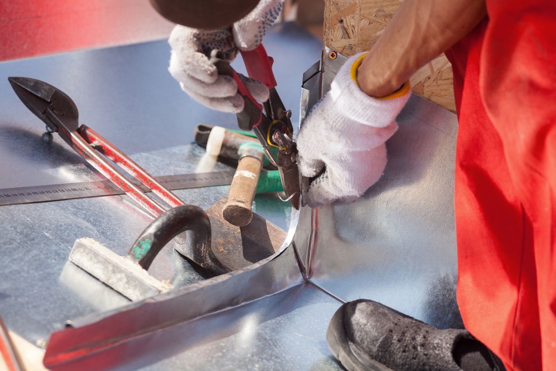 Personne portant des gants blancs utilisant des cisailles à métaux pour découper une feuille de métal.