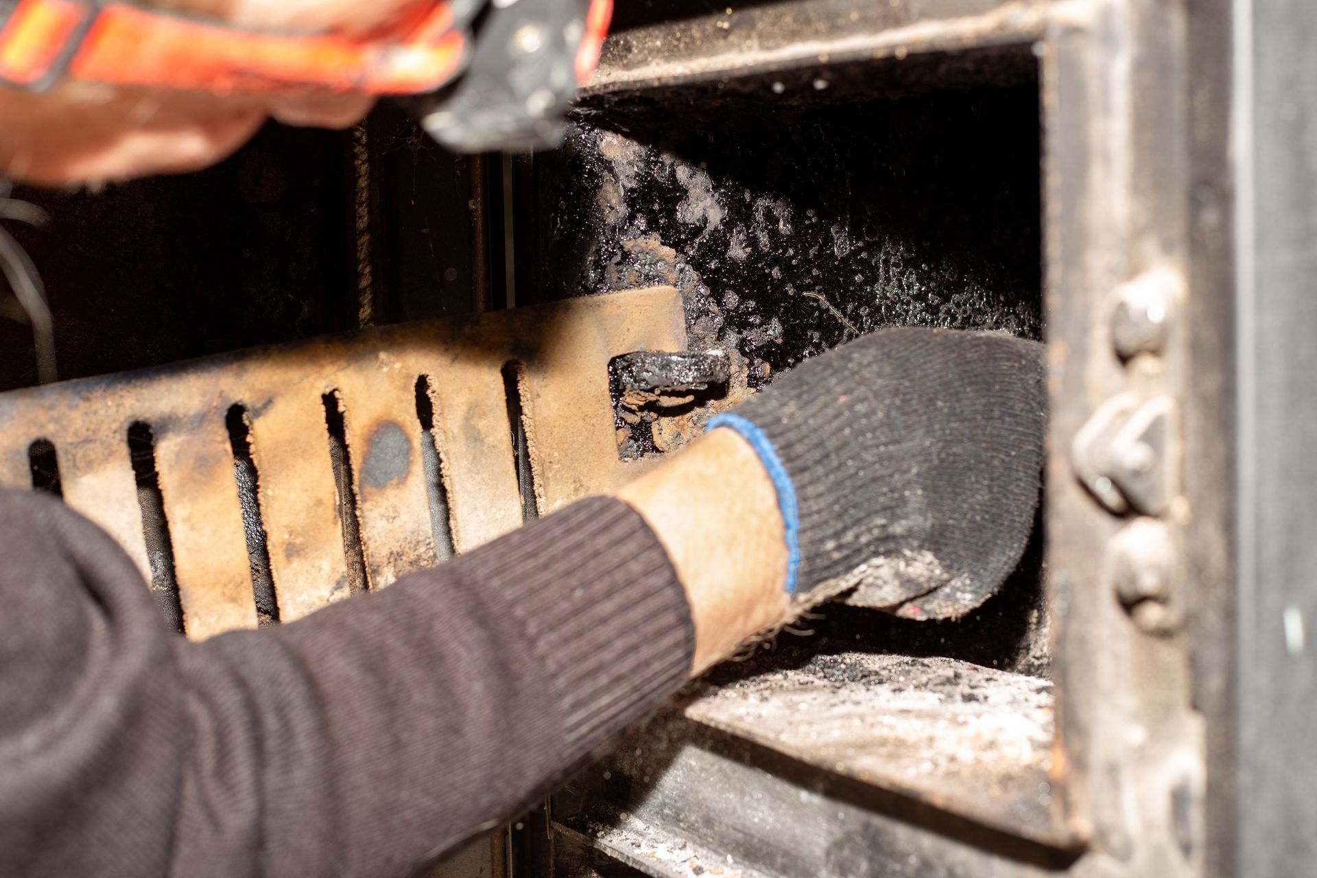 Nettoyage à la main (avec des gants) de l'intérieur d'un poêle à bois, où l'on voit des cendres et des débris.