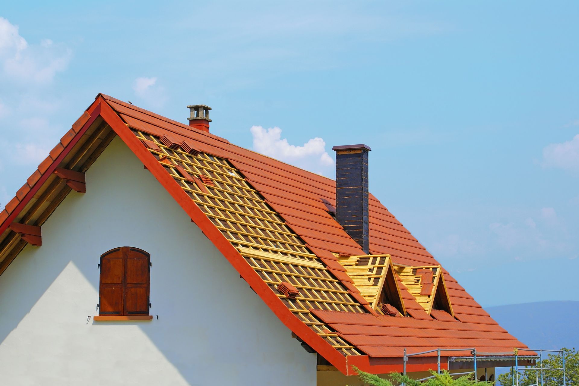 Maison au toit de tuiles rouges, une partie des tuiles manquantes laissant apparaître les poutres en bois, sous un ciel bleu.
