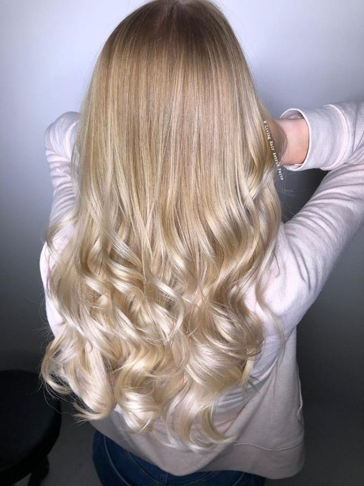 Eine Frau mit langen blonden Haaren trägt einen rosa Pullover und Jeans.