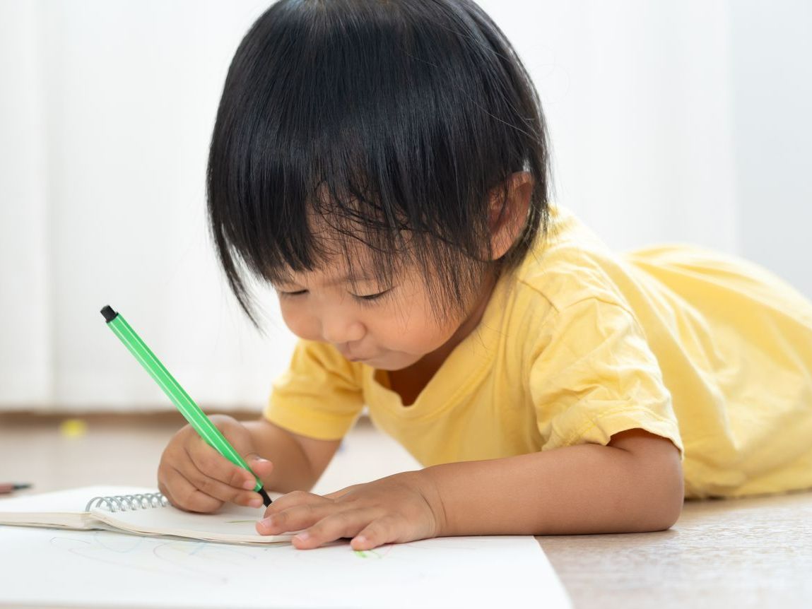 Un jeune enfant dessinant, couché sur le sol