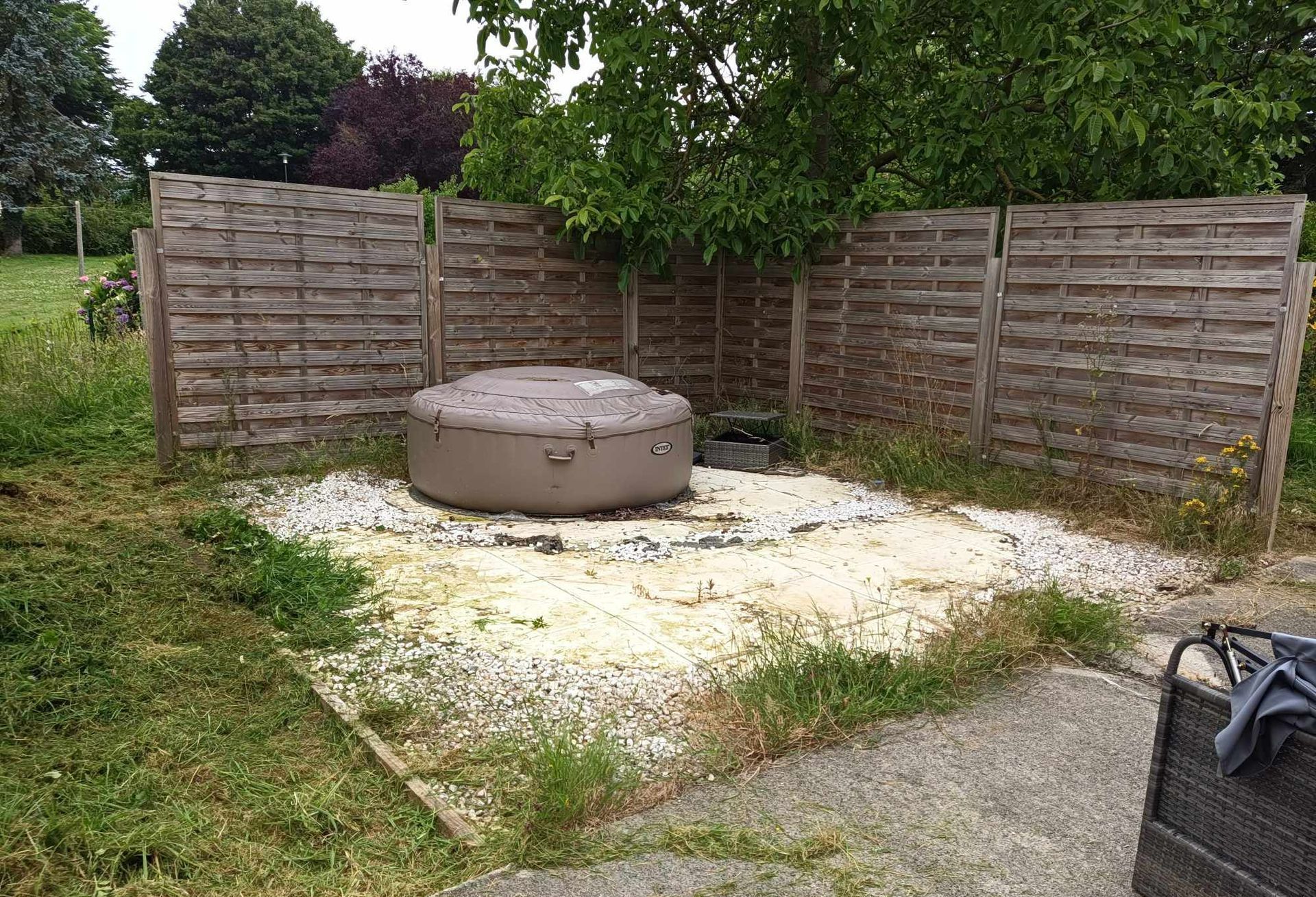 Petit jardin avec un brasero rond en béton posé sur du gravier, entouré d’une clôture en bois et d’une pelouse.
