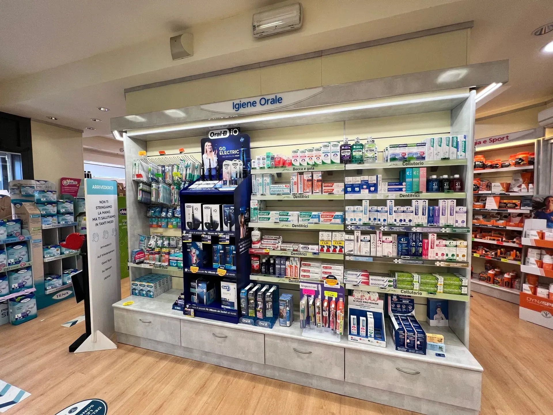 Corridoio della farmacia con medicinali da banco e prodotti per la salute su scaffali e un espositore a pavimento