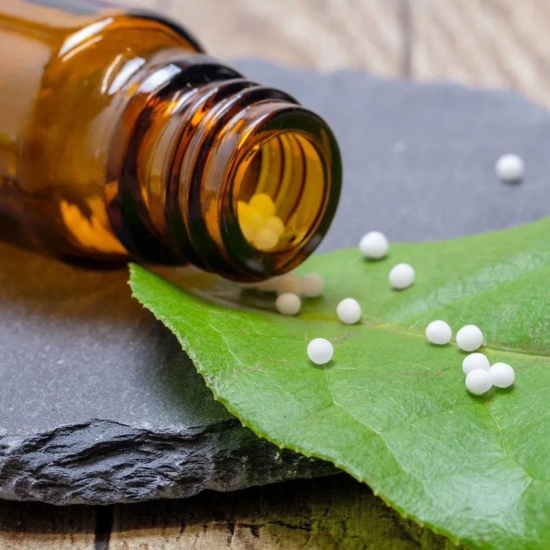 Flacone di medicinale color ambra con compresse bianche su foglie verdi e una pietra nera.