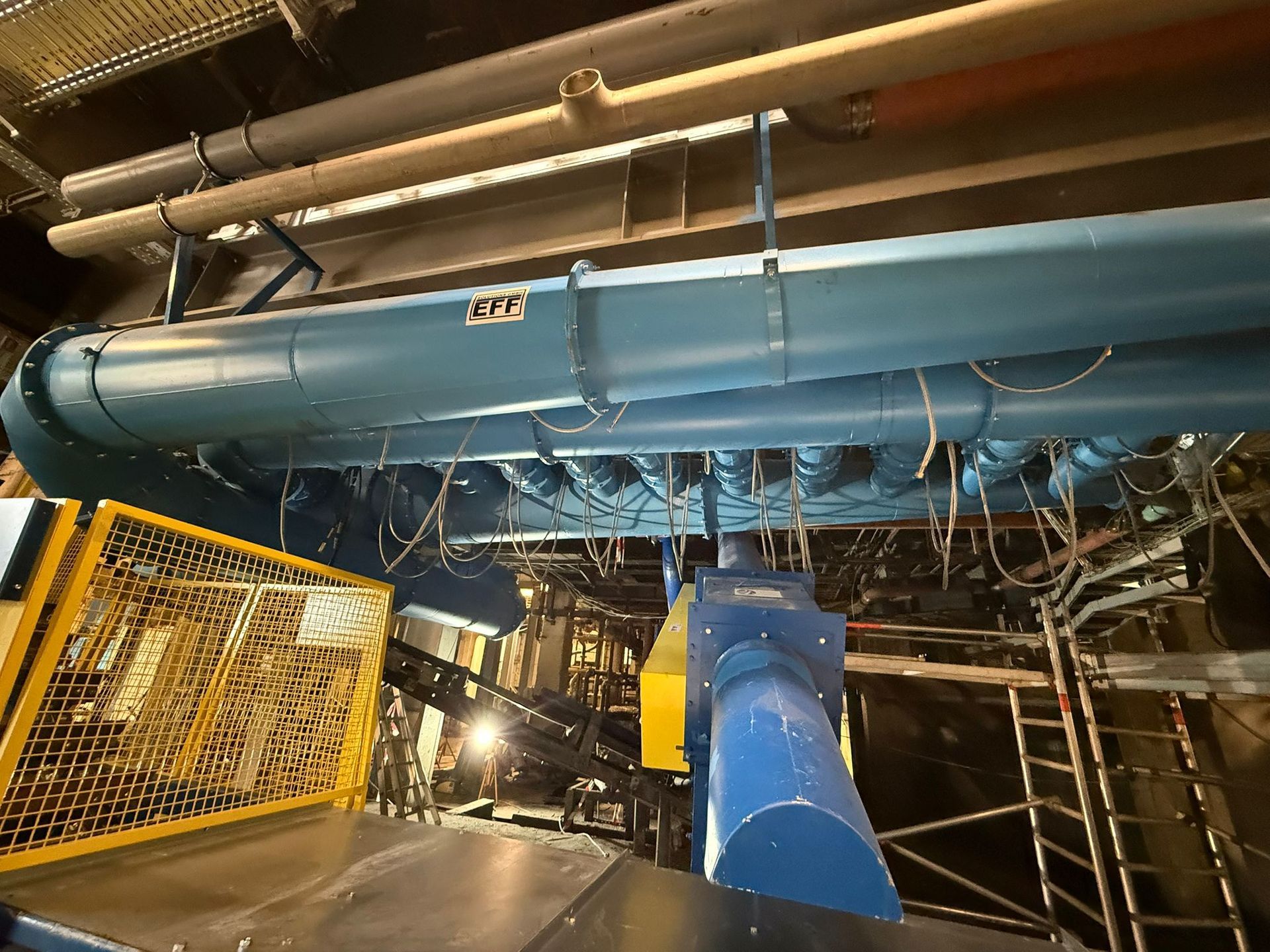 Blaues industrielles Lüftungssystem mit freiliegenden Kabeln und Metallgittern.