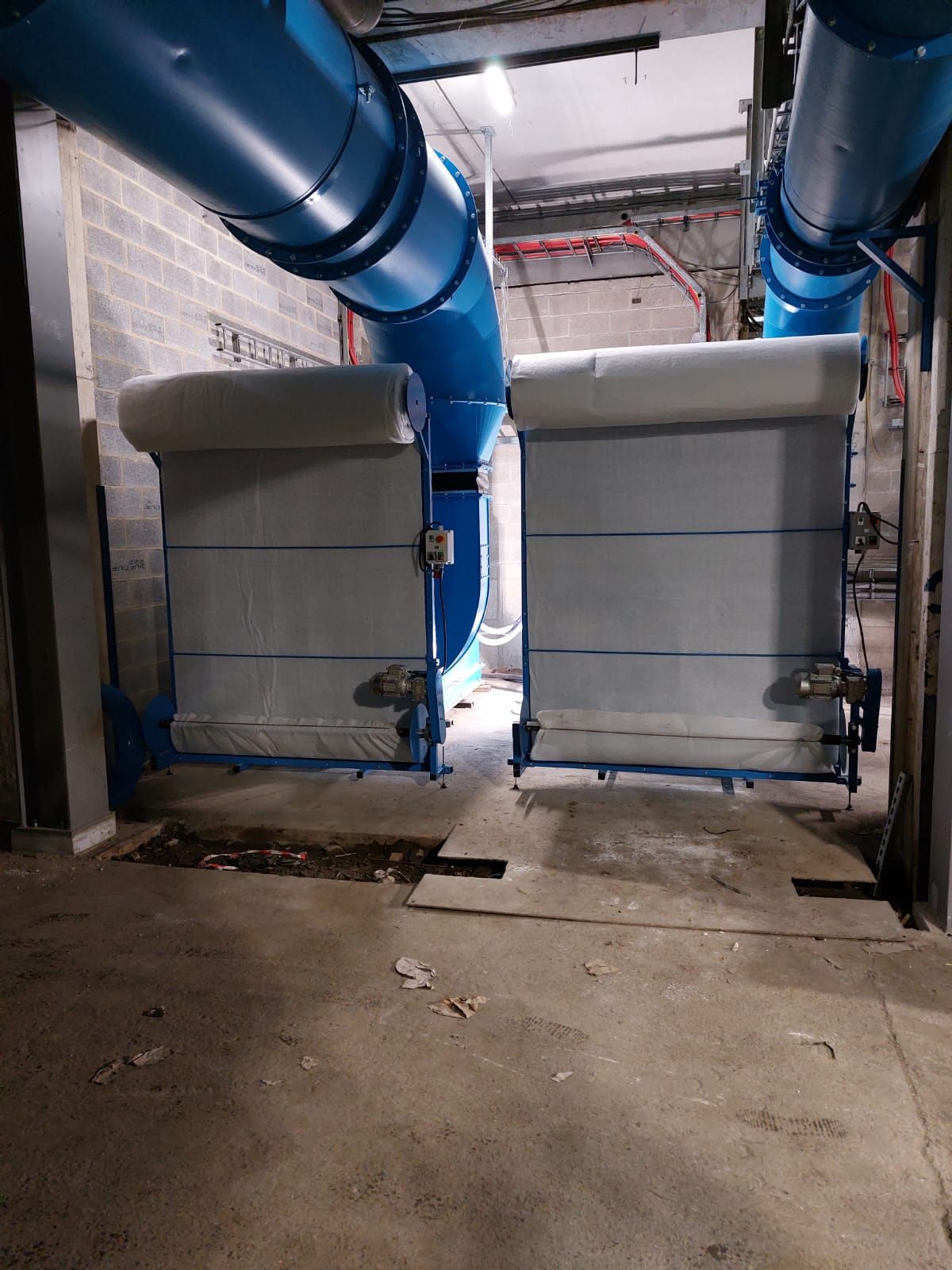 Zwei graue Industrie-Rolltore, blaue Rohre darüber, Betonboden und eine Wand aus Zementsteinen.