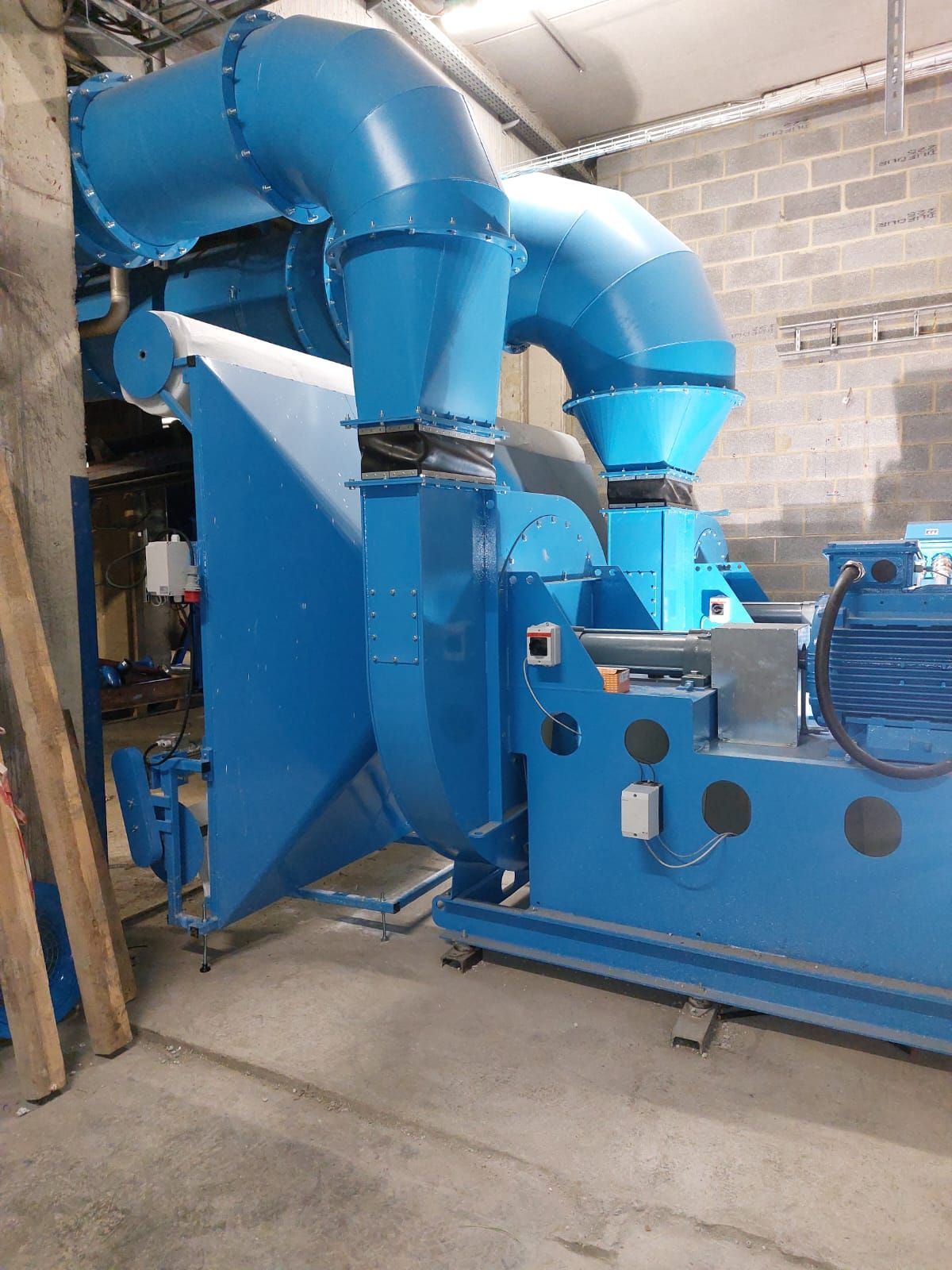 Blaue industrielle Lüftungsanlagen vor einer grauen Backsteinmauer.