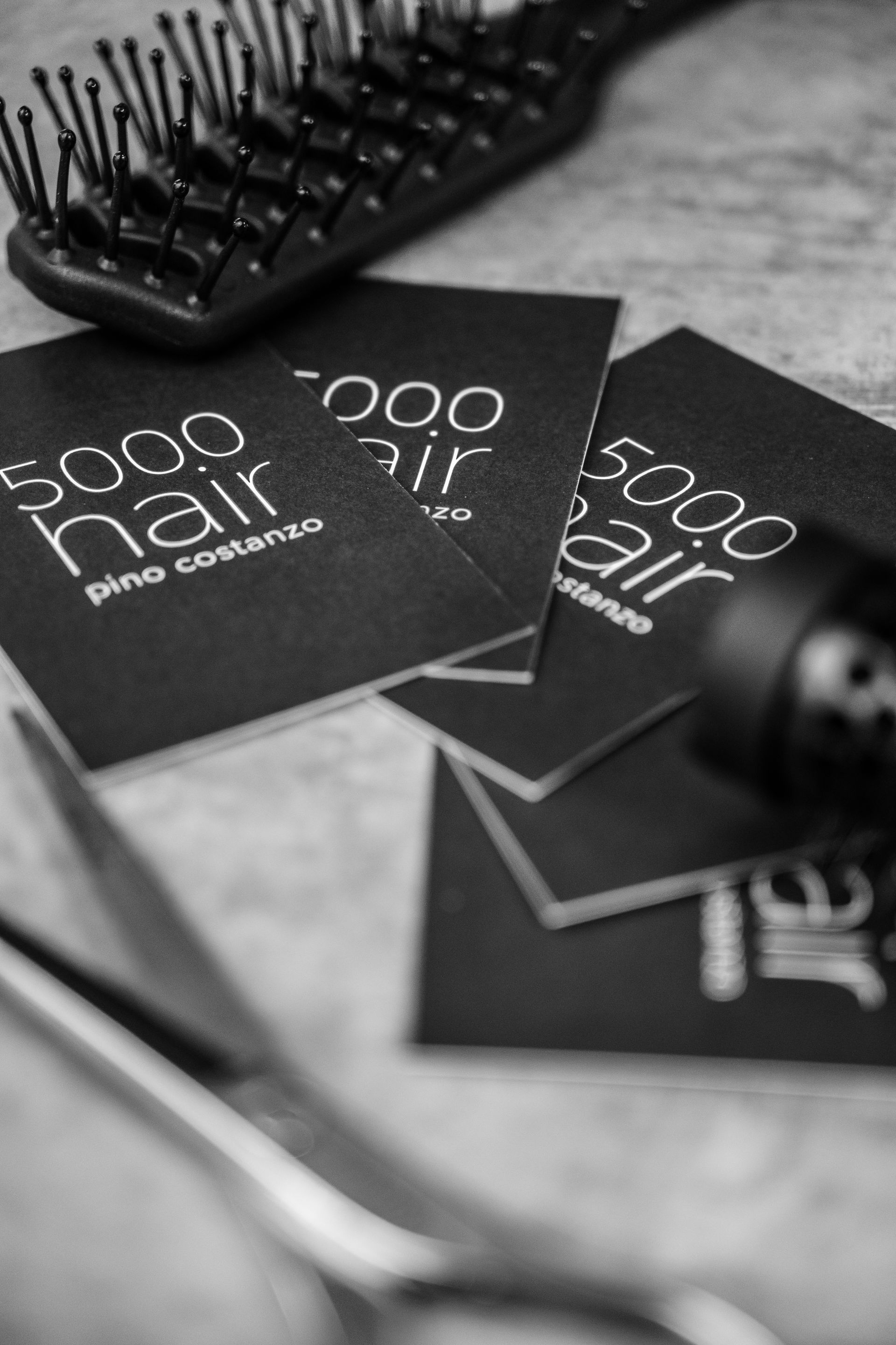 Schwarz-Weiß-Foto von Friseurutensilien und Visitenkarten: Kamm, Schere und Karten mit dem Logo „5000 Hair“.
