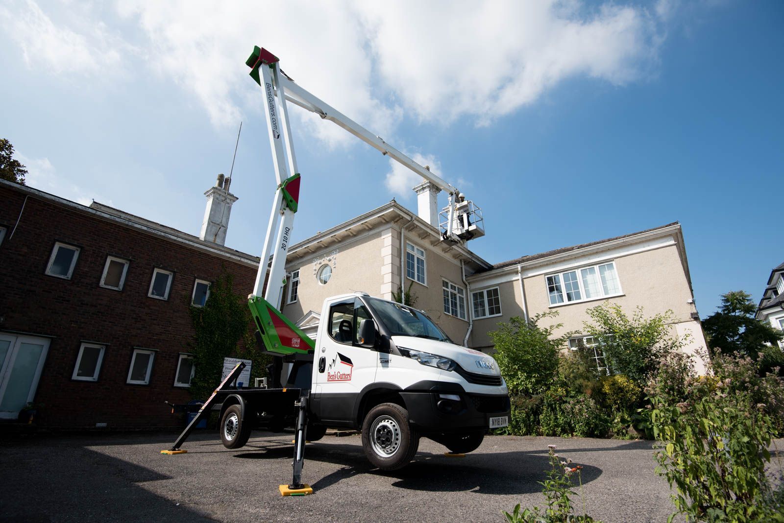 White utility van with crane lifting equipment beside a building in a sunny courtyard