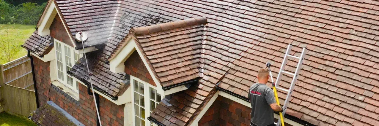Worker on a roof fixing tiles with ladders beside a house