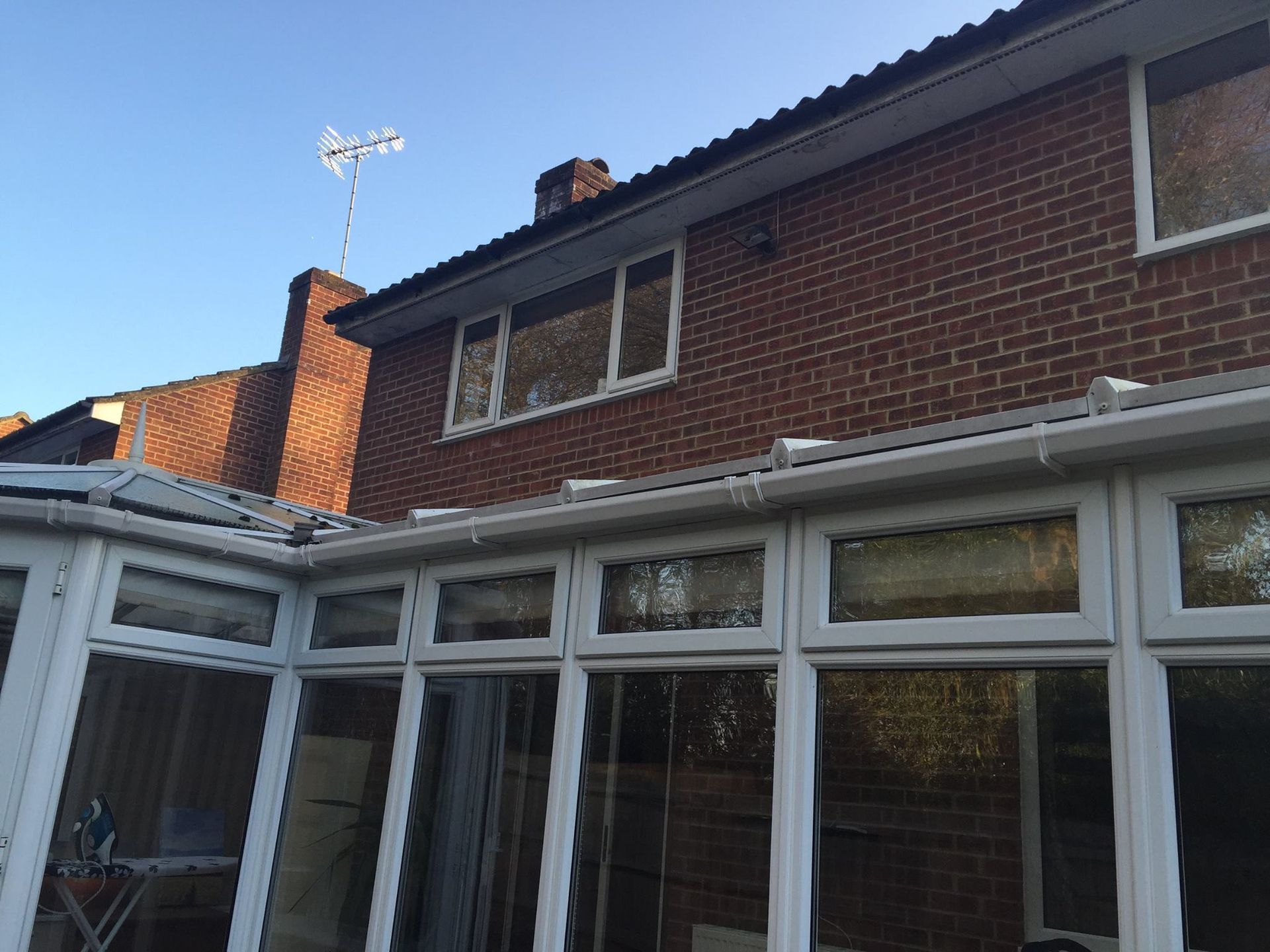 Brick house exterior with white conservatory roof and windows under a blue sky