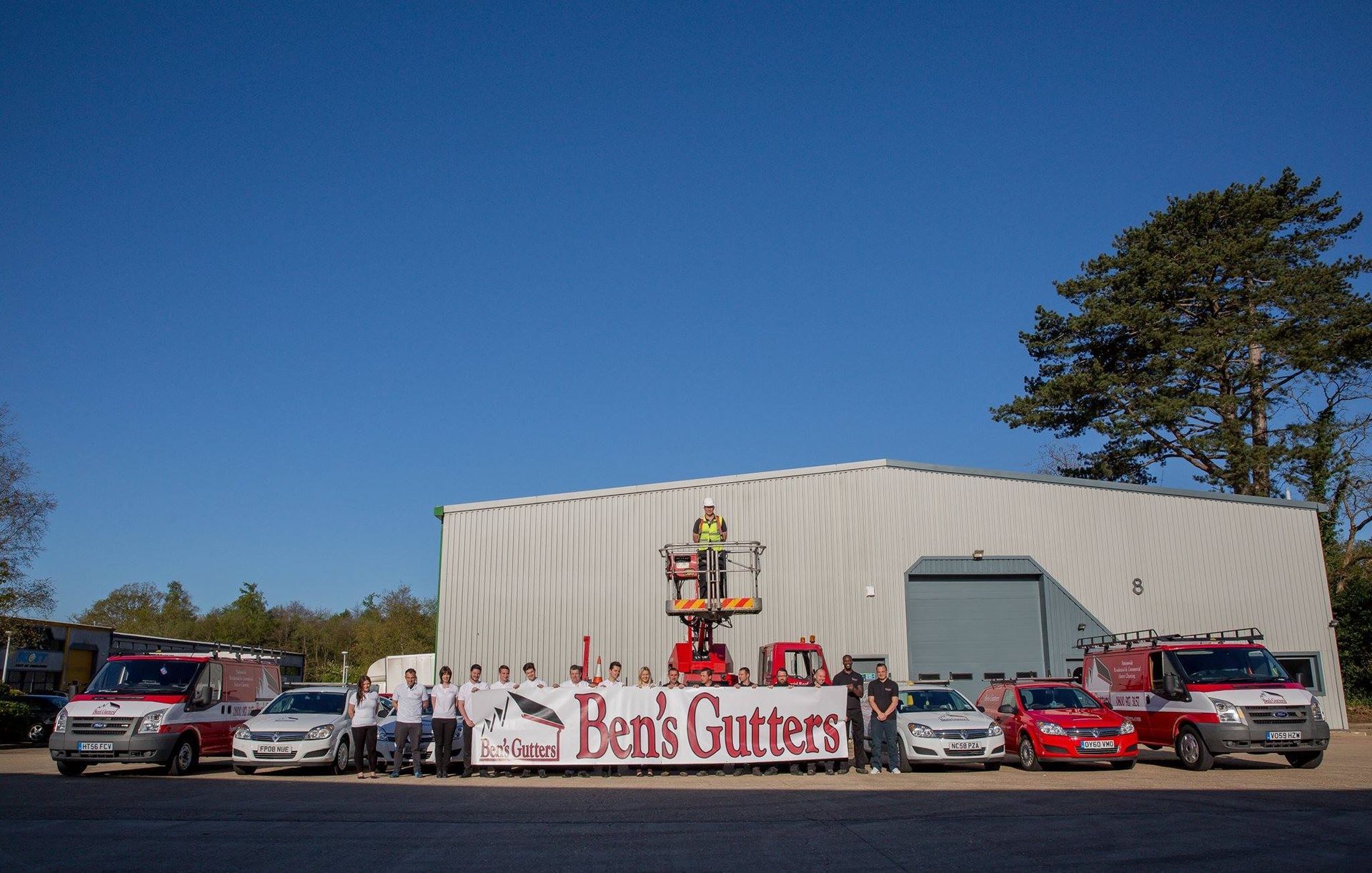 Ben’s Gutters service truck and workers outside a white warehouse under a blue sky