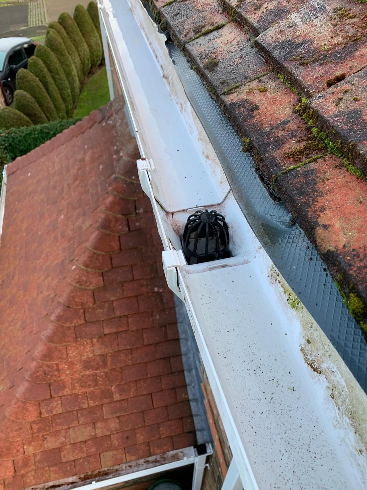 Roof gutter with a black clog near red-tiled rooftops and greenery