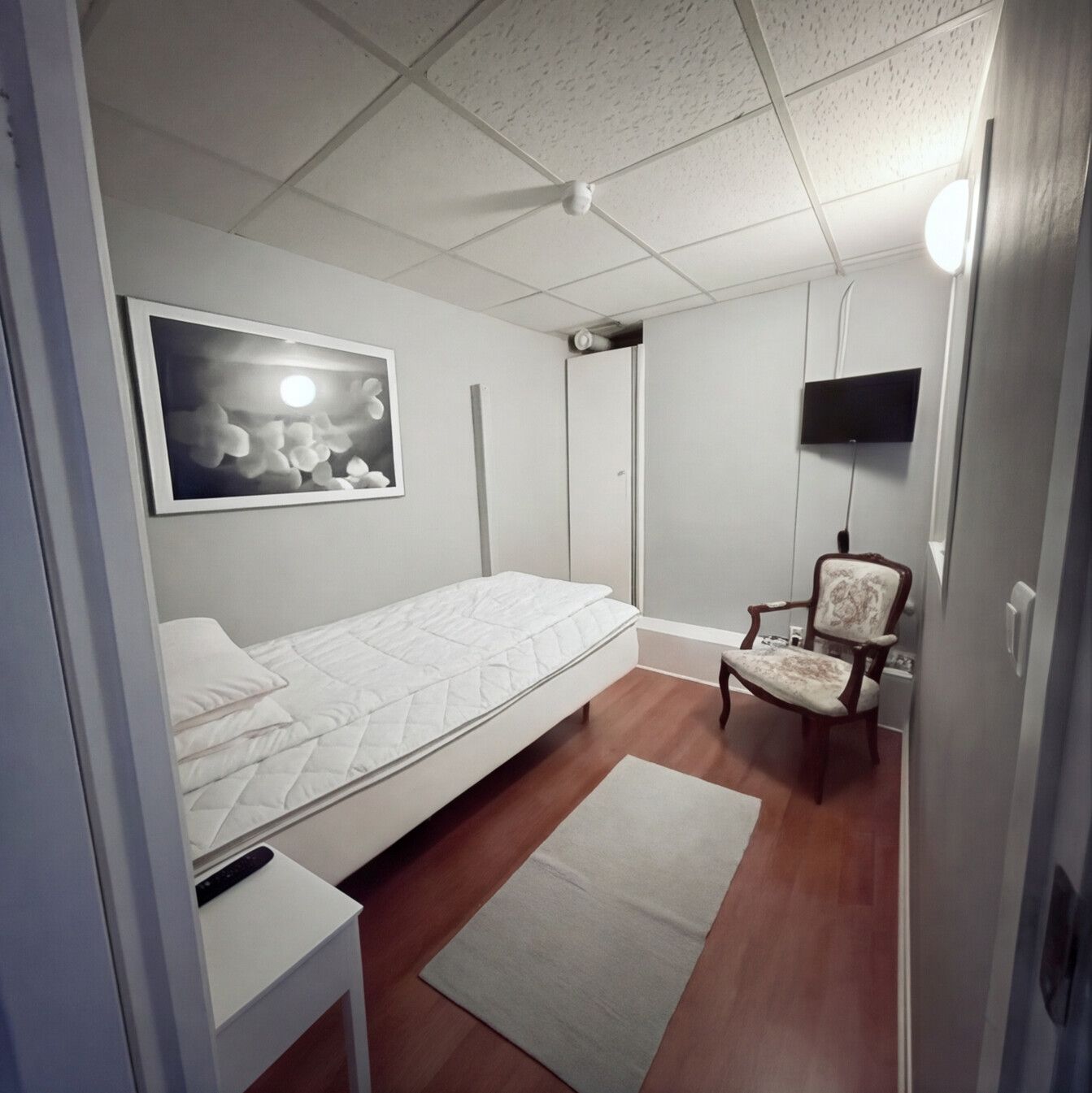 Hemtrevligt enkelrum med en enkelsäng, en klassisk karmstol och en tavla på väggen.