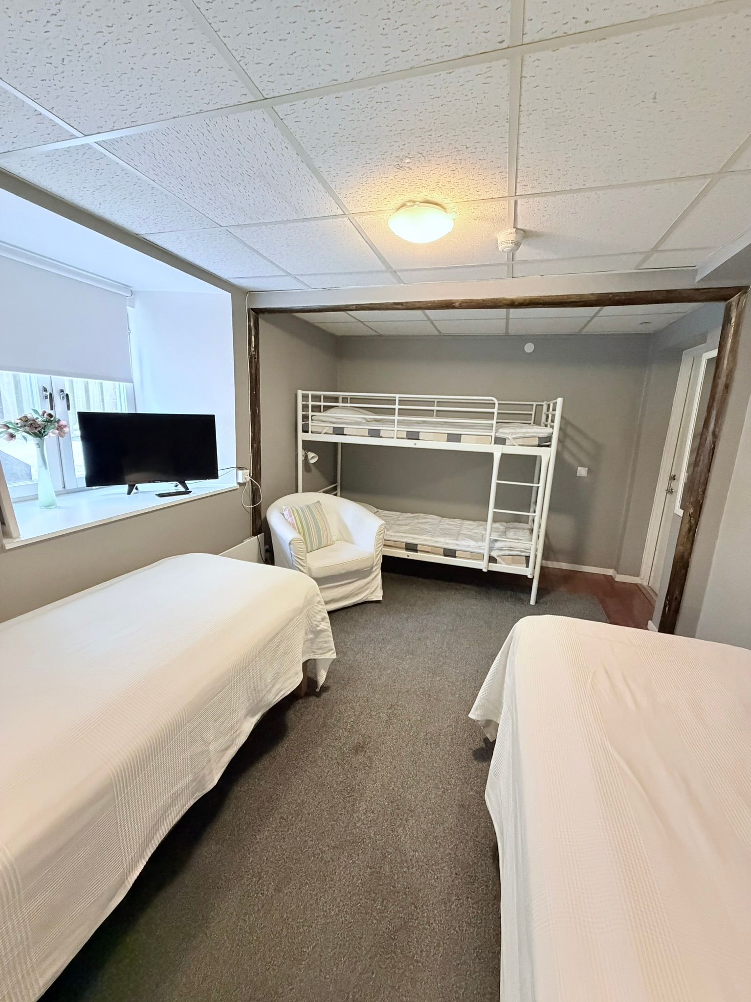 Familjerum med en vit fåtölj, en enkelsäng och en våningssäng.