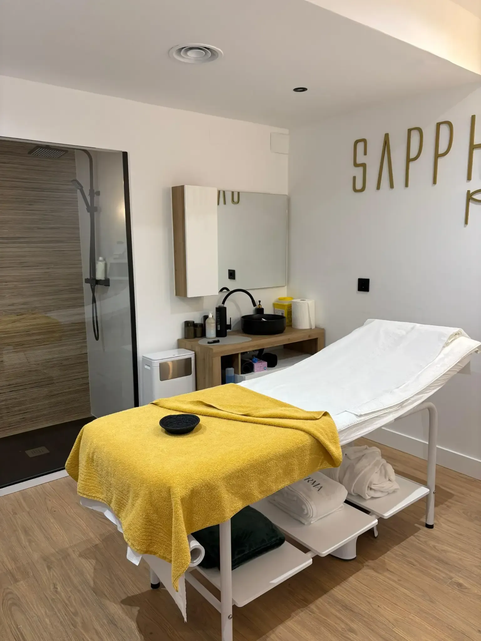 Sala de tratamiento con paredes blancas, mesa de masajes y lavabo negro.