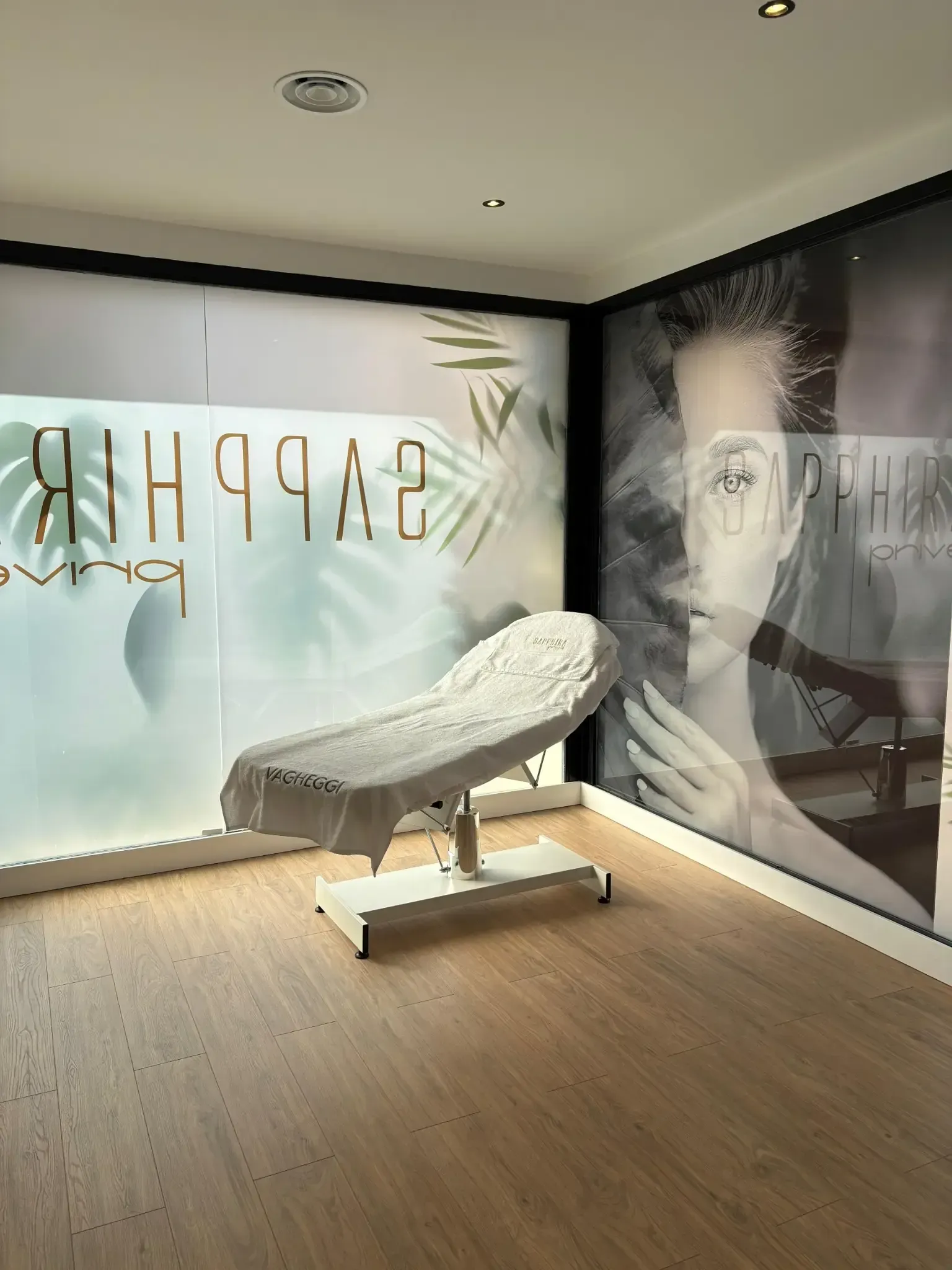 Sala de tratamientos de spa con mesa de masajes, piso de madera clara y grandes obras de arte decorativas en la pared.