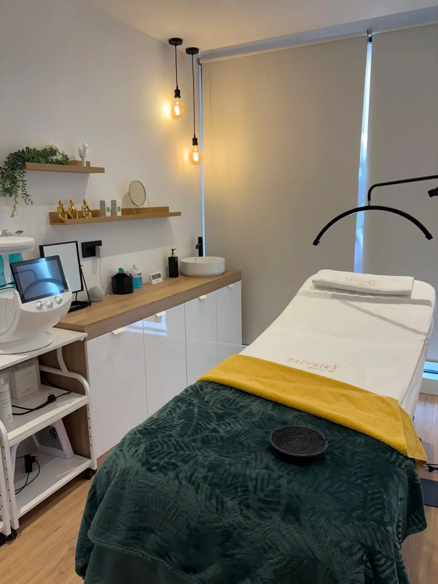 Sala de tratamientos de spa con una cama cubierta de verde y amarillo, estantes y equipos de belleza.