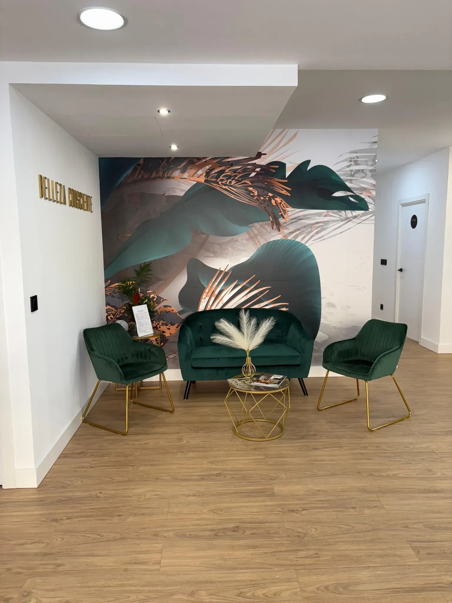 Área de espera con asientos de terciopelo verde, detalles dorados y mural abstracto.