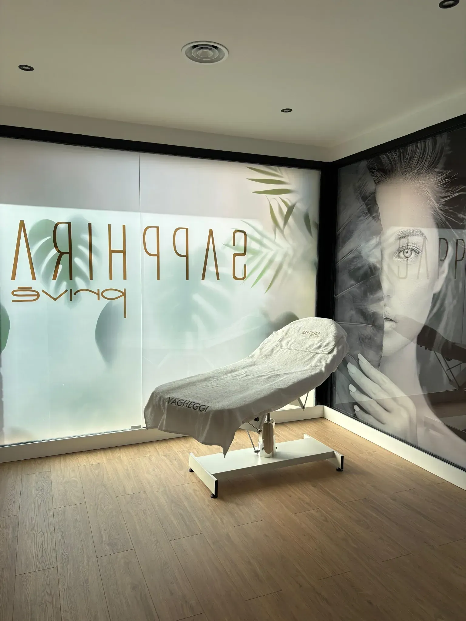 Sala de tratamiento con camilla estética, ventana esmerilada con logo y retrato en la pared.