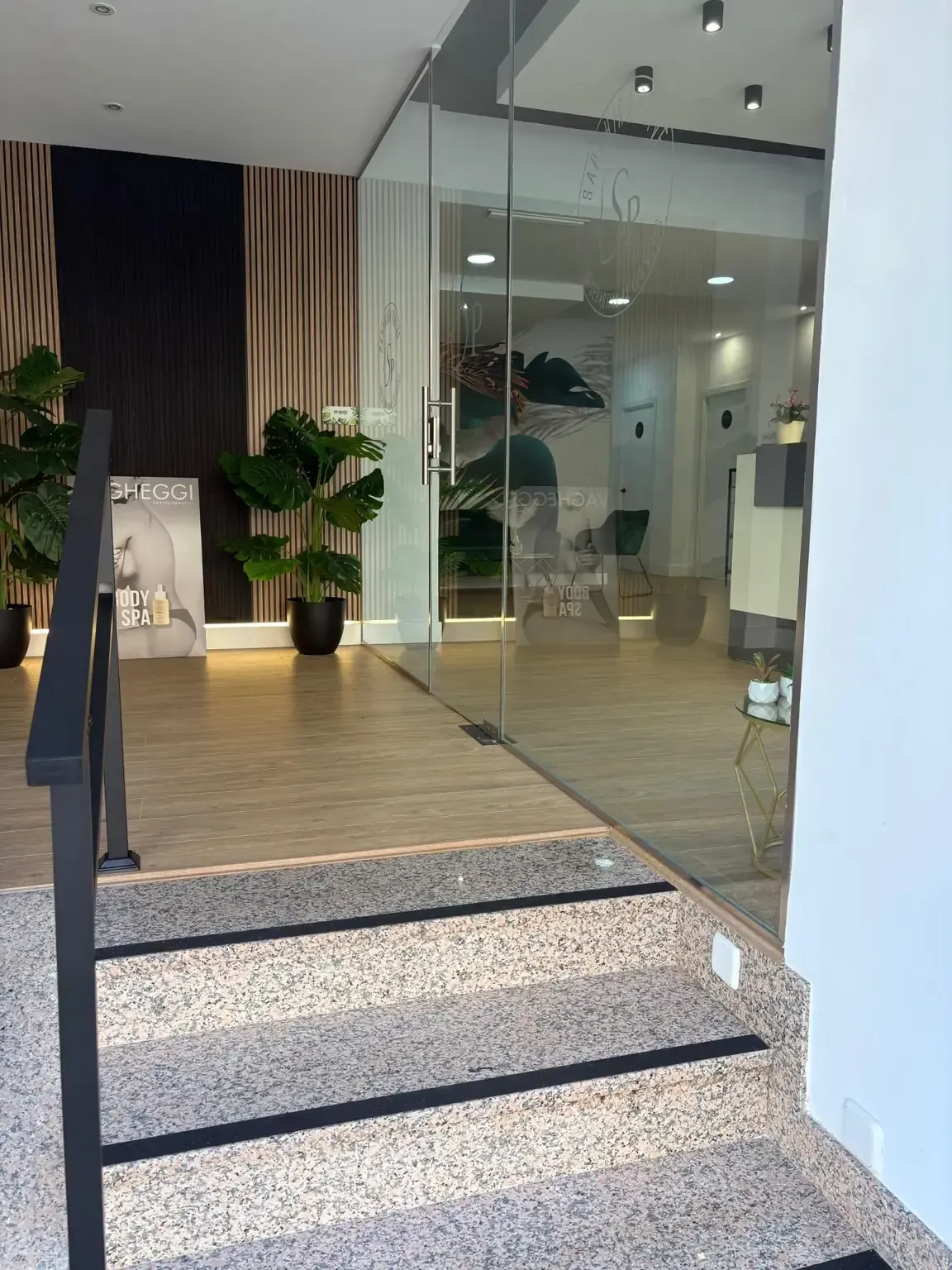 Entrada con puerta de vidrio al interior con escaleras, con pasamanos negro y piso moteado.