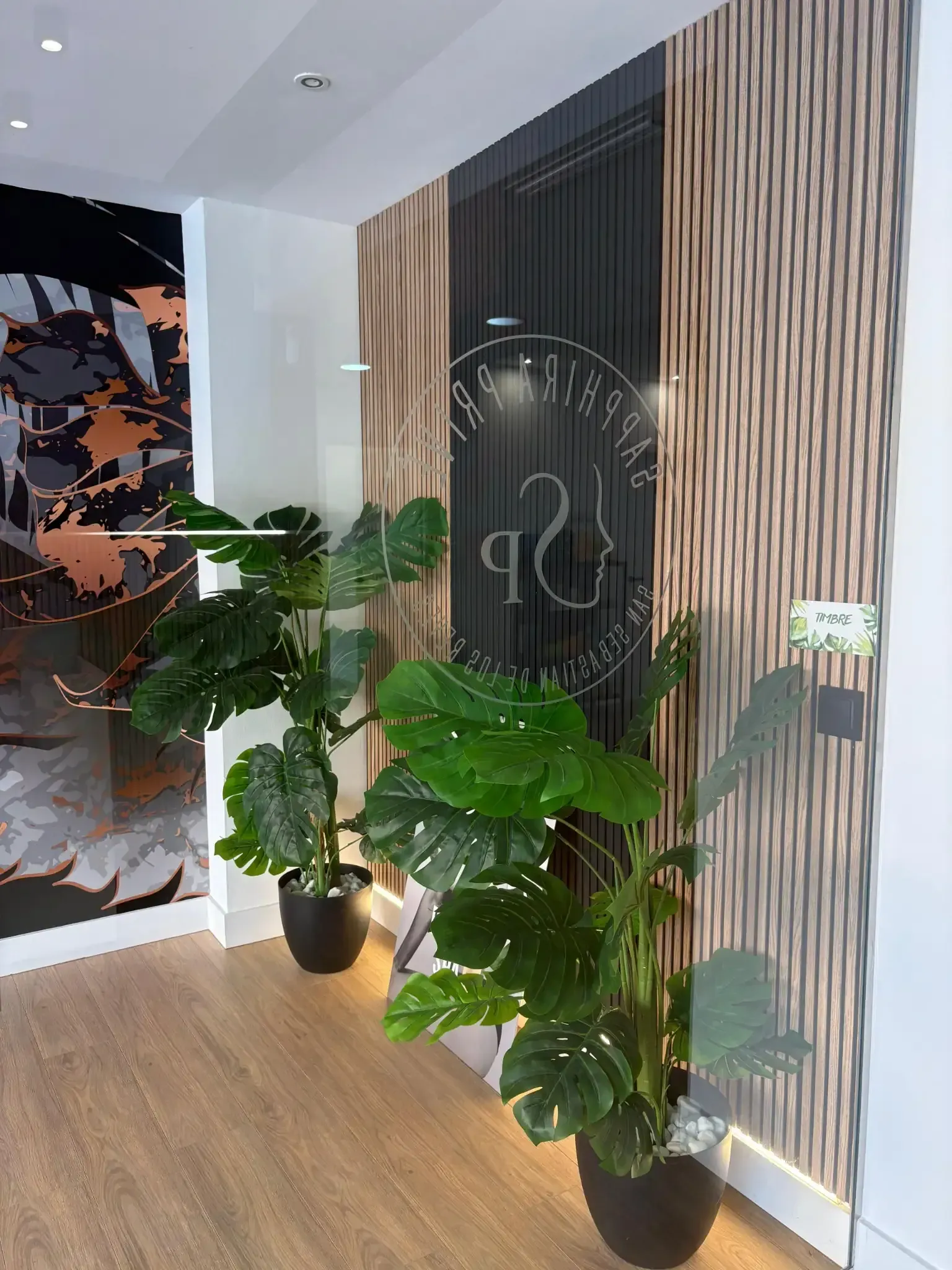 Una entrada con plantas en macetas, paneles de madera y una puerta de vidrio esmerilado con un logotipo.