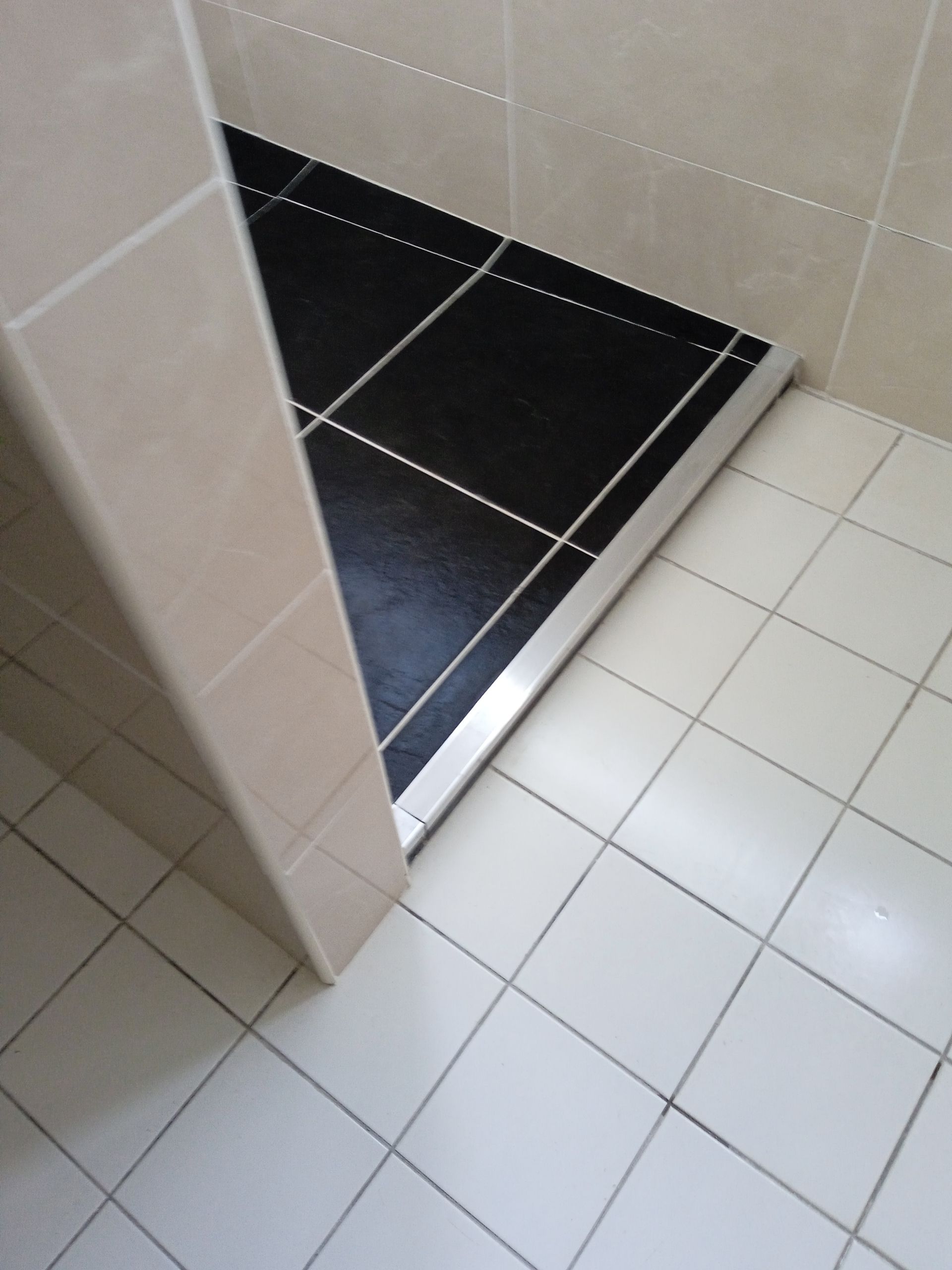 Douche avec receveur carrelé noir et murs en carrelage blanc.